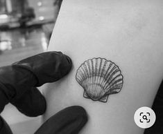 a small shell tattoo on the back of a woman's left arm, next to a glove