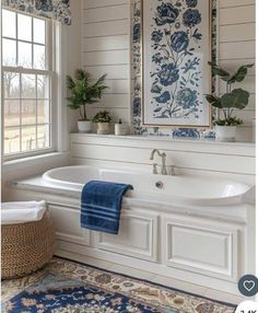 a white bath tub sitting under a window next to a rug and potted plants