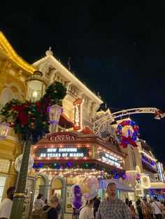 people are walking around in front of a building with christmas decorations on the sides and lights all around it