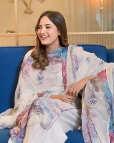 a woman sitting on top of a blue couch wearing a white and pink sari