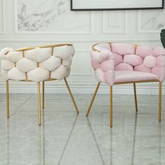 two pink and gold chairs sitting next to each other in front of a white wall