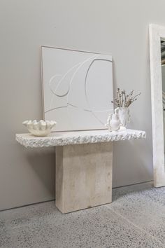 a white vase sitting on top of a table next to a framed art piece with flowers in it