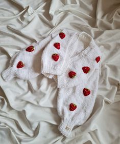 two white sweaters with strawberries on them are laying on a bed covered in sheets