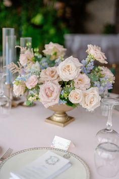 a table topped with a vase filled with pink and white flowers next to wine glasses