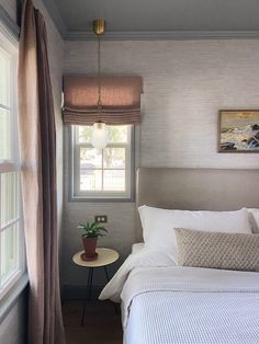 a white bed sitting next to a window with curtains on top of it and a small table in front of it