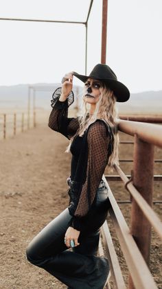 a woman in a cowboy hat leaning against a fence with her hand on her hip