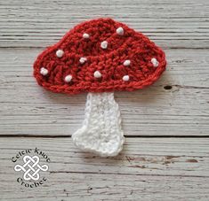 a crocheted mushroom hat with white dots on it sitting on a wooden surface