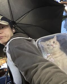 a person holding an umbrella with a cat in the back seat on their arm and behind them