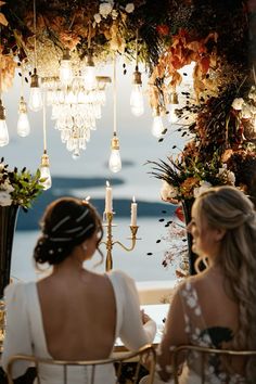 two women sitting at a table in front of a chandelier with hanging lights