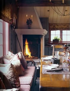 a dining room table with place settings in front of an open fire burning in the fireplace