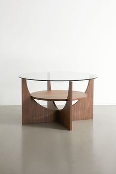 a table with a glass top and wooden base on the floor in front of a white wall