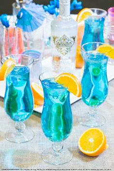 three glasses filled with blue liquid sitting on top of a table next to orange slices