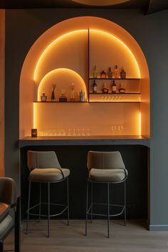 two bar stools sitting in front of a counter with bottles on it and shelves