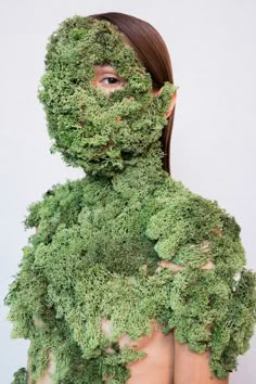 a woman is covered in moss and has her face partially hidden by the grass covering her body