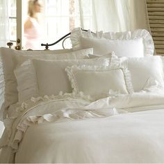 a bed with white sheets and ruffled pillows