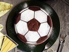 a chocolate and white soccer ball cake on a green plate with silverware next to it