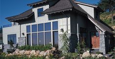 a large house with lots of windows next to a rock wall and green plants on the front lawn