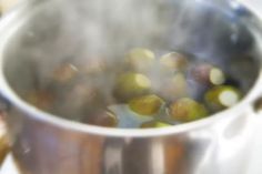 a metal pot filled with green olives on top of a stove burner and steam rising from the bottom