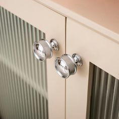 two knobs on the side of a white cabinet with metal doors and blinds behind them