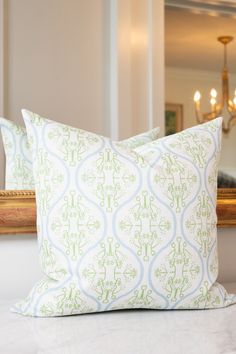 a white and green pillow sitting on top of a bed next to a mirror with a chandelier in the background