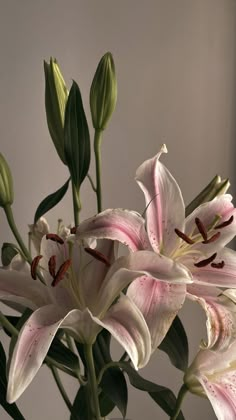 a vase filled with white and pink lilies on top of a wooden table next to a window