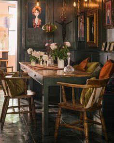 a dining room table with chairs and pictures on the wall above it, along with vases filled with flowers