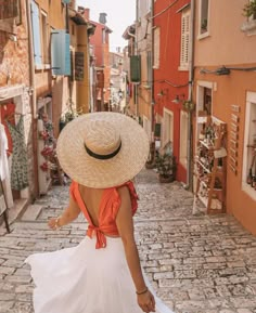 a woman wearing a large hat walking down a cobblestone street