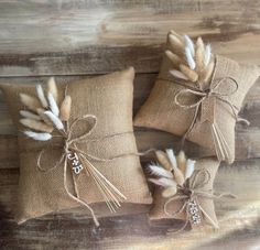 three burlap pillows with white feathers tied to them on a wooden table top