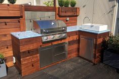 an outdoor bbq with grill and sink on top of wooden deck next to building