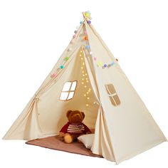 a teddy bear sitting in front of a teepee tent with lights on the side