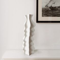 a tall white vase sitting on top of a shelf next to a framed photo and painting