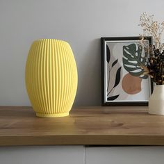 a yellow vase sitting on top of a wooden shelf next to a framed photograph and flowers