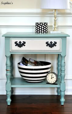 a blue table with a black and white striped bowl on it, next to a clock