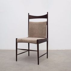 a wooden chair with a beige seat and back rest on concrete flooring in front of a white wall