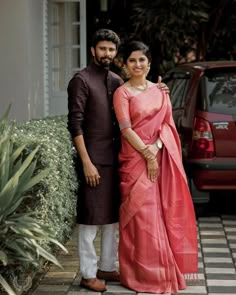 a man and woman standing next to each other in front of a red car on the street