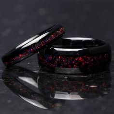 two black rings with red and blue flecks on them sitting on a reflective surface