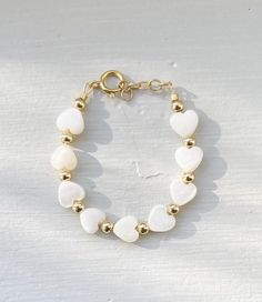 This darling bracelet creates a timeless symbol of love and beauty! Featuring luminous pearl heart beads with gleaming gold-plated accents including a 14K gold-filled clasp.  THERE ARE NO RETURNS OR EXCHANGES FOR WRONG SIZE. To ensure proper sizing, please measure your baby's wrist before you purchase. Use a soft measuring tape tightly and add 1/2" to find the correct size. Every bracelet includes a ½" of extension loops for growth and wiggle room as well.  WARNING: CHOKING HAZARD Never leave a child unattended with a bracelet on. Dainty White Personalized Heart Bracelet, White Heart Bracelet With Pearl Charm, White Heart-shaped Bracelet With Pearl Charm, Dainty Personalized White Heart Bracelet, Hypoallergenic White Pearl Bracelet In 14k Gold Filled, Cute Pearl Jewelry With Heart Beads, Dainty White Pearl Bracelet For Birthday, Gold Heart-shaped Beaded Bracelet For Birthday, White Dainty Pearl Bracelet For Birthday