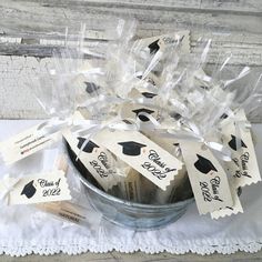 graduation party favors in a bucket on a white tablecloth with ribbons and tags attached to them