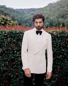 a man in a tuxedo standing next to a hedge