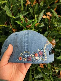 someone is holding up a denim hat with embroidered flowers on it