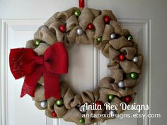 a burlock wreath with ornaments hanging on the front door, decorated with red ribbon