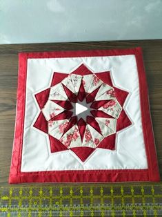 a red and white quilted wall hanging on a wooden floor next to measuring tape