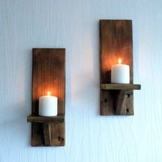 two wooden wall sconces with lit candles on them against a white painted wall