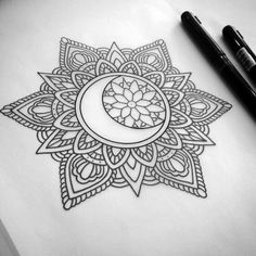 a drawing of a crescent moon with intricate designs on paper next to two black pens