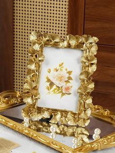 a gold frame with flowers and pearls is on a table next to a white cloth