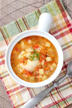 a white bowl filled with soup on top of a checkered cloth next to a spoon