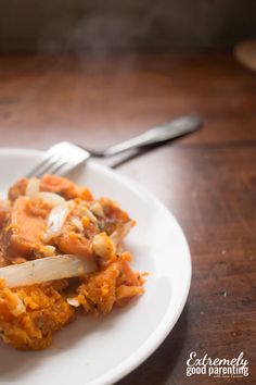 a white plate topped with food on top of a wooden table next to a fork