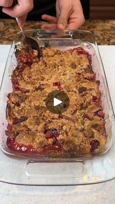 someone is cutting into a berry crumbled dessert in a glass dish on a table