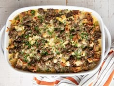 a casserole dish with meat, cheese and vegetables in it on a striped towel