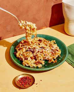 a green plate topped with pasta and toppings next to a measuring cup on a table